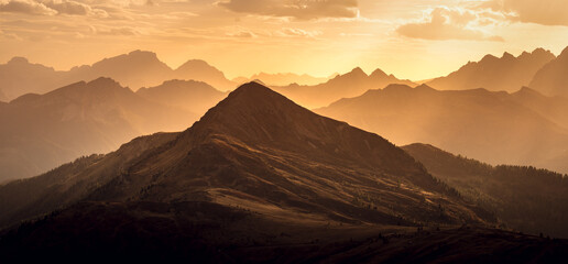 Italian Dolomites in colorful golden sunrise. Misty Alpine mountains in haze. Silhouettes of...