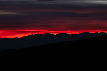 Dark red sky at Italian Dolomites with mountain peaks in distance. Twillight hour at Italian Alps. 