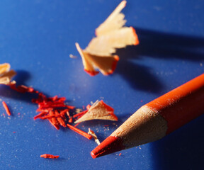 Orange sharpened colored pencil on blue background with wood shavings