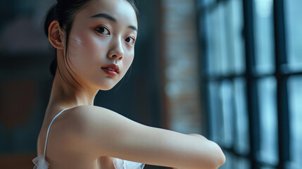 Young Asian ballet dancer in a studio practicing poses looking gracefully at the camera, copy space