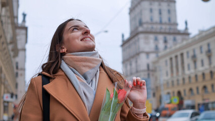 Fototapeta premium Portrait of a happy shade girl with a tulip in the background of the city in the cold season.