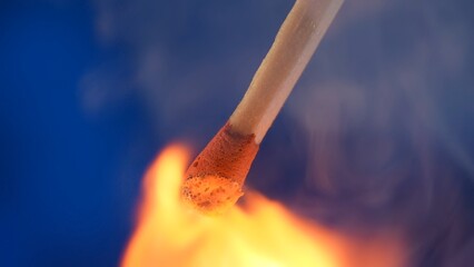 Macro shot of a burning match against a blue studio background. The flame of the burning match...