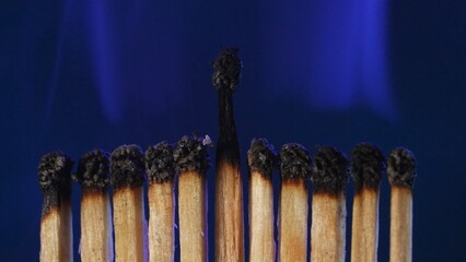 Row of black charred matches and light white smoke on dark studio background. The matches have...
