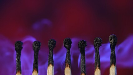Row of black charred matches and light white smoke on dark studio background. The matches have extinguished and left a trail of smoke. Macro shot.