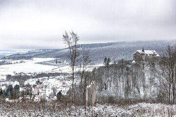 Winter landscape with a gloomy sky and an ancient castle on a hill in the middle of a forest