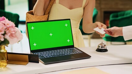 Laptop with greenscreen display on hotel front desk next to lounge area, modern isolated chromakey...