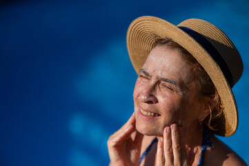 Portrait of an older woman applying sunscreen to her face while on vacation. 