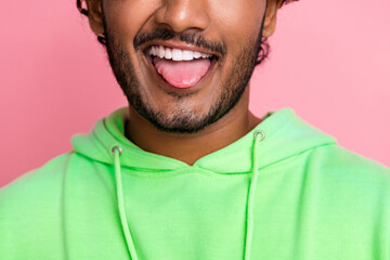 Close up cropped photo of funny young guy in green hoodie stick out protrude tongue childish behavior isolated on pink color background