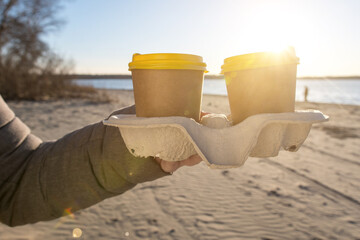 stand with cups of coffee in hand on the background of the beach. eco-friendly packaging