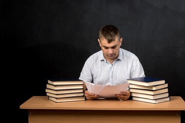 a man of Slavic appearance reads papers at a desk or table. teacher on the background of a slate wall