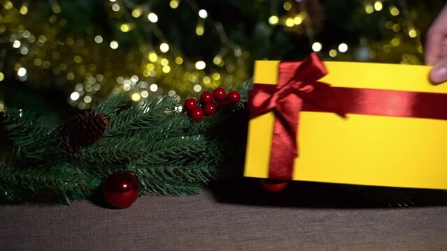 A hand places a yellow gift certificate with a red satin ribbon and a bow on a brown tablecloth on a New Year's branch