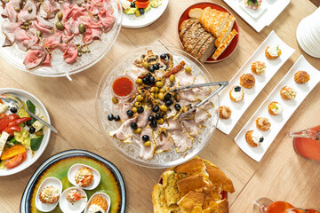 Scene of a table with appetizers. Top view on white wooden background. Board with appetizers, meat with capers, cheese, assorted holiday dishes. Olives, Italian bread.