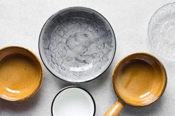 Overhead view of different plates dinnerware on a marble countertop, top view of brown ramekin, grey plate and white cup
