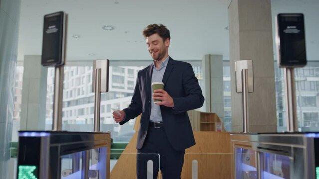 Manager opening automatic gates passing into modern office building with coffee 