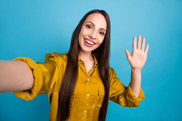 Photo of adorable excited lady wear yellow shirt recording video vlog waving arm hi isolated blue...