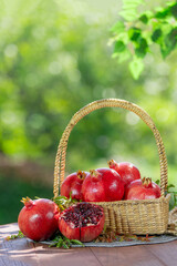 Pomegranate in wooden basket on wooden table in garden, Pomegranate with slices on blurred greenery background.
