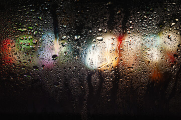 Raindrops on the window. Drops of water on the glass. Abstract background. Storefront lights. Texture of drops. Selective focus