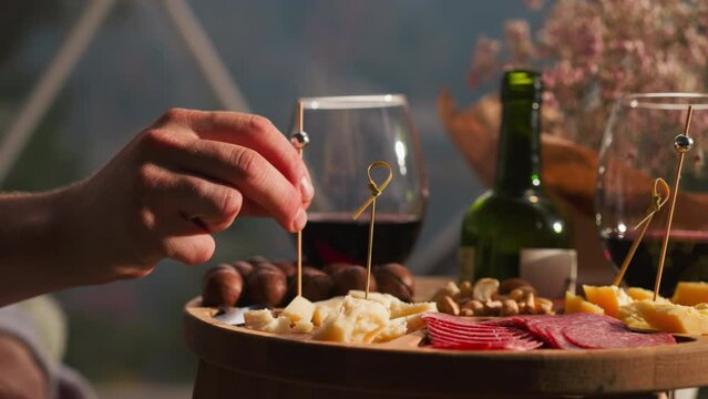 Man impales cheese onto skewer at small table closeup. Gourmet wants to taste new sort of cheese at dinner in restaurant. Snack plate for guests
