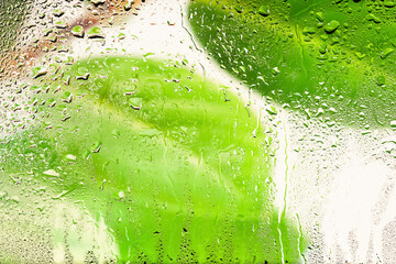 Raindrops on the window. Drops of water on the glass. Abstract background. Green leaves. Texture of drops