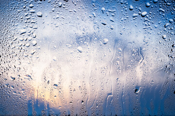 Raindrops on the window. Water drops on glass. Abstract background. Blue sky with clouds. Texture of drops. Selective focus