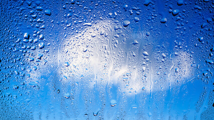 Raindrops on the window. Drops of water on the glass. Abstract background. Blue sky with clouds. Texture of drops. Selective focus