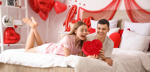 Young couple with gift lying in bedroom on Valentine's Day