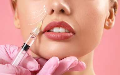 Young woman receiving filler injection in face against pink background, closeup