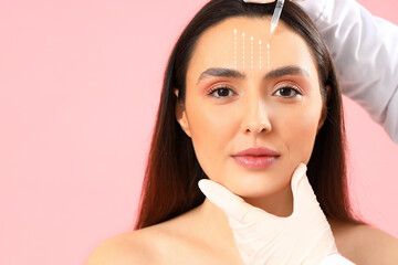 Young woman receiving filler injection in face against pink background