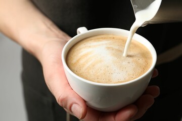 Woman pouring milk into cup of coffee on grey background, closeup