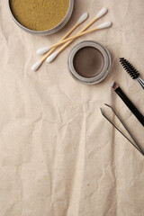 Flat lay composition with eyebrow henna and tools on crumpled paper. Space for text