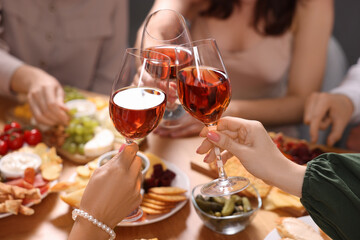 People clinking glasses with rose wine above wooden table, closeup