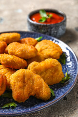 Plate with delicious nuggets, bowl of ketchup and herbs on grey grunge table, closeup
