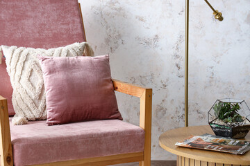 Pink armchair with cushions and florarium on coffee table near white grunge wall, closeup