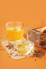 Glass with flax oil and bowl of seeds on orange background