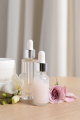 Fototapeta na wymiar Bottles of cosmetic serum and beautiful flowers on wooden table