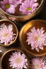 Tibetan singing bowls with water and beautiful flowers on wooden table, flat lay