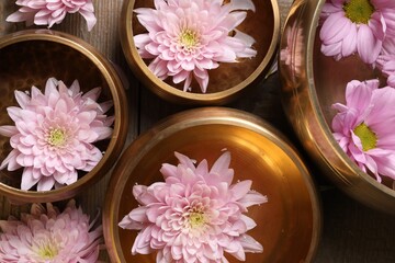 Fototapeta na wymiar Tibetan singing bowls with water and beautiful flowers on wooden table, flat lay