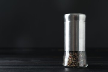 Pepper shaker on black wooden table, closeup. Space for text