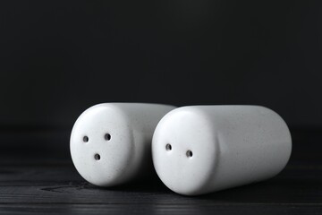 Pepper and salt shakers on black wooden table, closeup