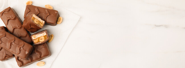 Chocolate candy bars with caramel, nuts and nougat on white marble table, flat lay. Banner design with space for text