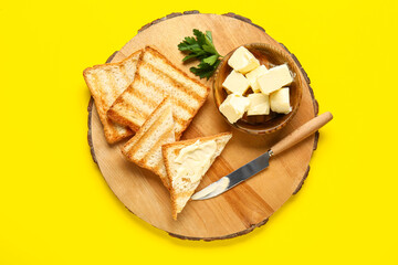 Wooden board with toasts and bowl of butter on yellow background