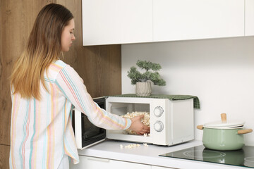 Pretty young woman making popcorn in microwave oven at modern kitchen