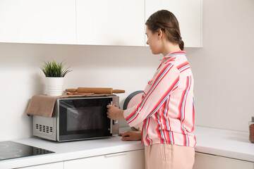Pretty young woman heating food in microwave oven at home - obrazy, fototapety, plakaty