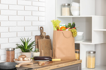 Paper bag with different products and utensils on counter in kitchen