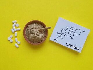 Structural chemical formula of cortisol (a steroid hormone) with white pills and ashwagandha powder. Cortisol is a stress hormone. Ashwagandha food supplements for stress and anxiety, medical concept.
