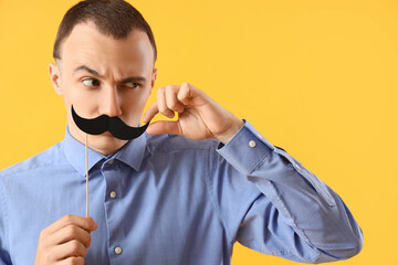 Funny young man with paper mustache on yellow background, closeup