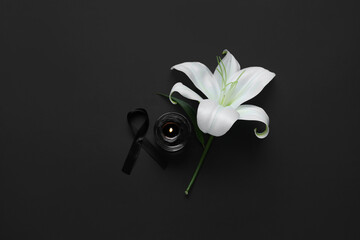 Beautiful lily flower with funeral ribbon and candle on black background