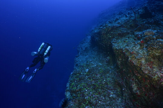 Scuba diver swim along a tropical wall near Maui, wearing a closed circuit rebreather. A rocky reef grows on the back wall at molokini crater.