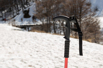 um bastão de esqui em pé na neve. O bastão é de cor vermelha e tem uma alça preta, tem marcas...