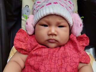 Cute Asian baby wearing a red dress and wearing a knitted hat, riding in a black stroller